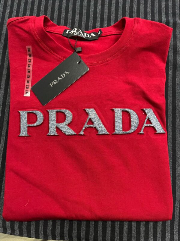 Camiseta com aplicação de logo Esta camiseta Prada é confeccionada em algodão e apresenta uma silhueta descontraída com decote careca. Na frente, um logo em alto relevo aparece para um sutil toque inconfundível.